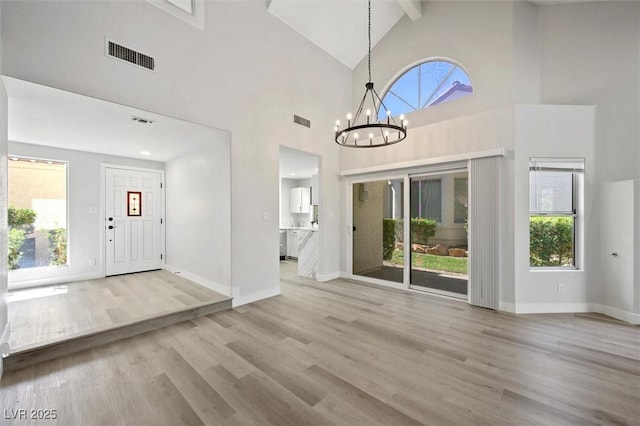 foyer entrance with visible vents, wood finished floors, high vaulted ceiling, plenty of natural light, and a chandelier