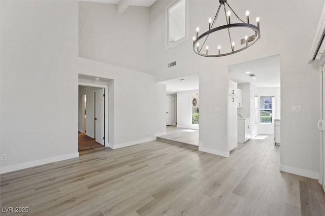 unfurnished living room with a towering ceiling, visible vents, baseboards, a notable chandelier, and light wood-style floors