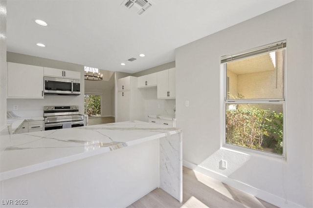 kitchen with light stone counters, light wood-style flooring, stainless steel appliances, white cabinetry, and visible vents