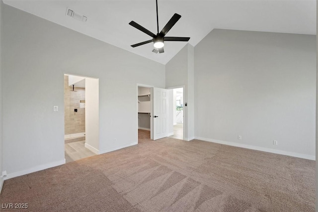 unfurnished bedroom featuring a walk in closet, visible vents, baseboards, high vaulted ceiling, and light carpet