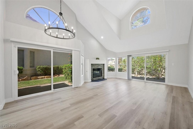 unfurnished living room with wood finished floors, baseboards, high vaulted ceiling, a fireplace with flush hearth, and a notable chandelier