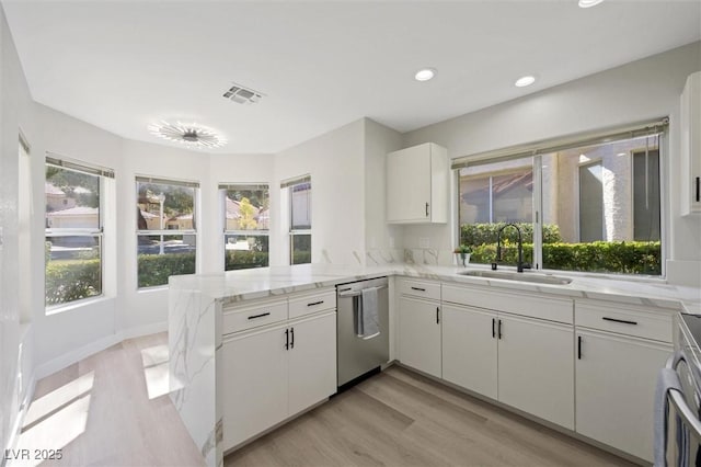 kitchen featuring visible vents, appliances with stainless steel finishes, a sink, light wood finished floors, and a peninsula