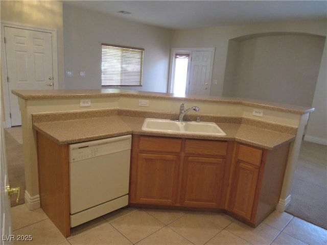 kitchen with brown cabinets, white dishwasher, light tile patterned flooring, a sink, and light countertops