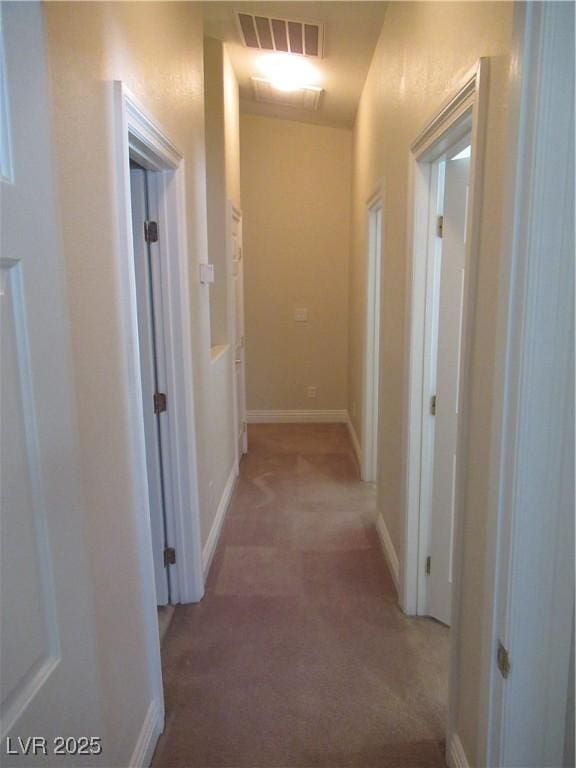hall featuring baseboards, visible vents, and light carpet