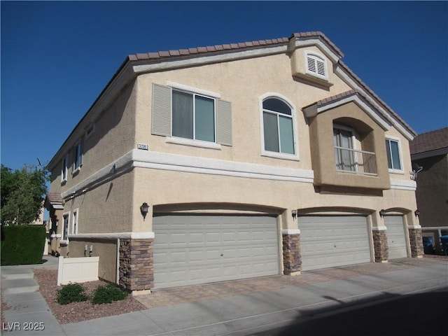 view of front of house featuring a garage, driveway, stone siding, and stucco siding