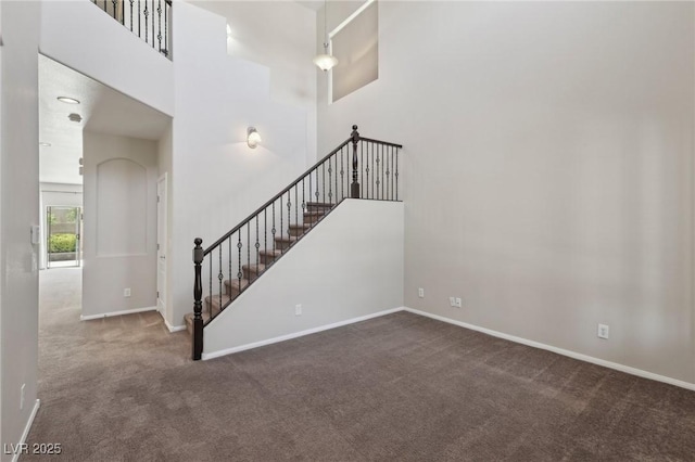 staircase featuring carpet floors, baseboards, and a high ceiling