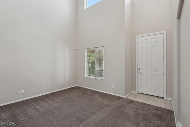 tiled entrance foyer featuring baseboards, carpet, and a towering ceiling