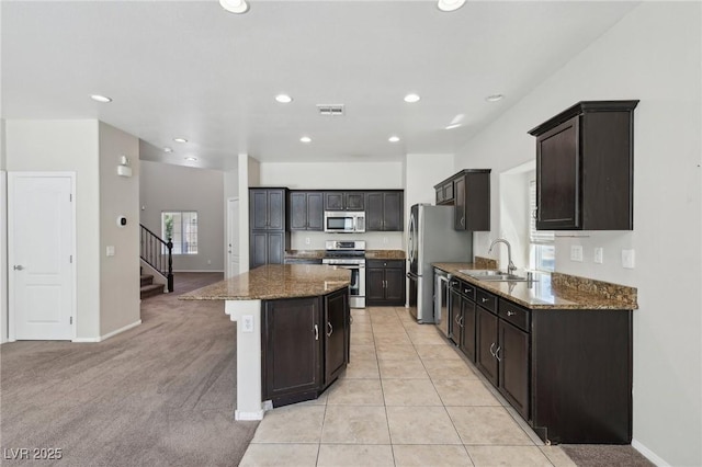 kitchen featuring appliances with stainless steel finishes, a sink, a center island, dark stone counters, and recessed lighting