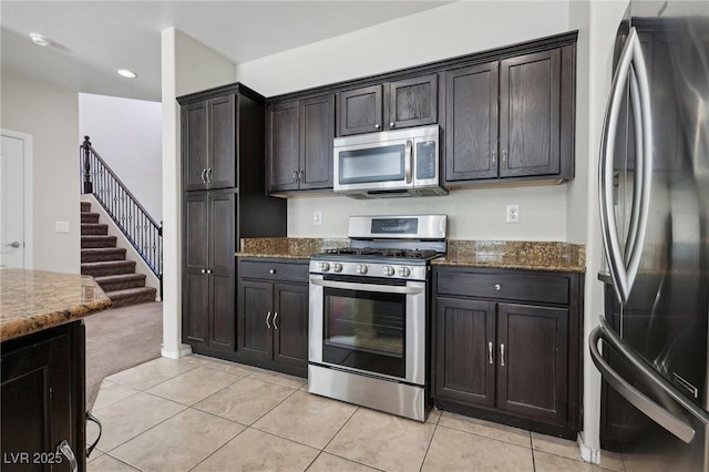 kitchen featuring dark brown cabinets, appliances with stainless steel finishes, light tile patterned floors, and dark stone countertops