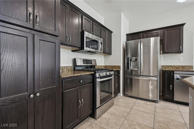 kitchen featuring dark stone counters, appliances with stainless steel finishes, dark brown cabinetry, and light tile patterned flooring