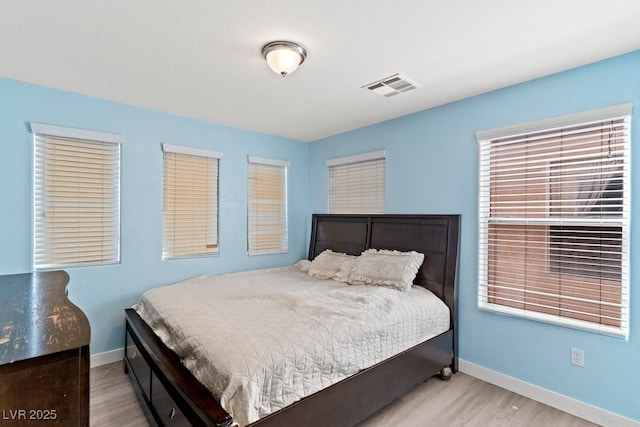 bedroom with baseboards, visible vents, and wood finished floors