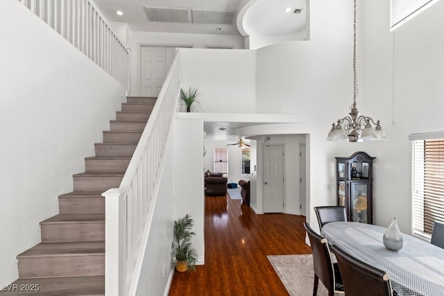 stairs with wood finished floors, a towering ceiling, and ceiling fan with notable chandelier