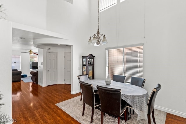 dining space with a towering ceiling, arched walkways, wood finished floors, baseboards, and ceiling fan with notable chandelier