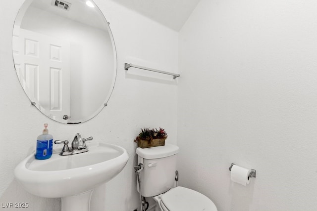 half bath with toilet, visible vents, and a sink