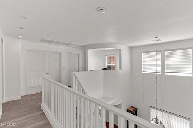 hallway featuring arched walkways, baseboards, an upstairs landing, light wood-type flooring, and visible vents