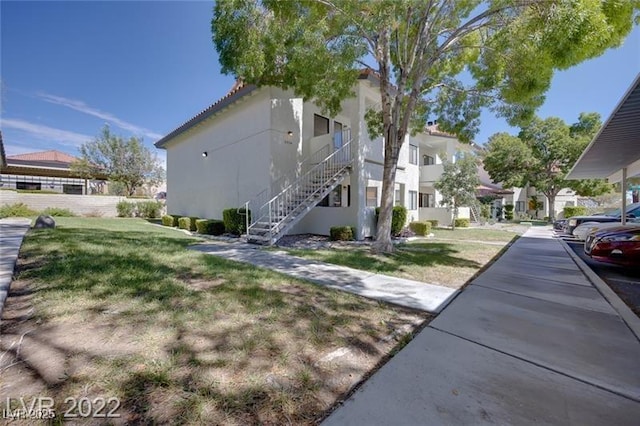 view of side of property featuring a lawn, stucco siding, and stairway