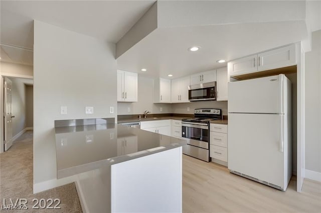kitchen featuring a peninsula, baseboards, white cabinets, a sink, and stainless steel appliances