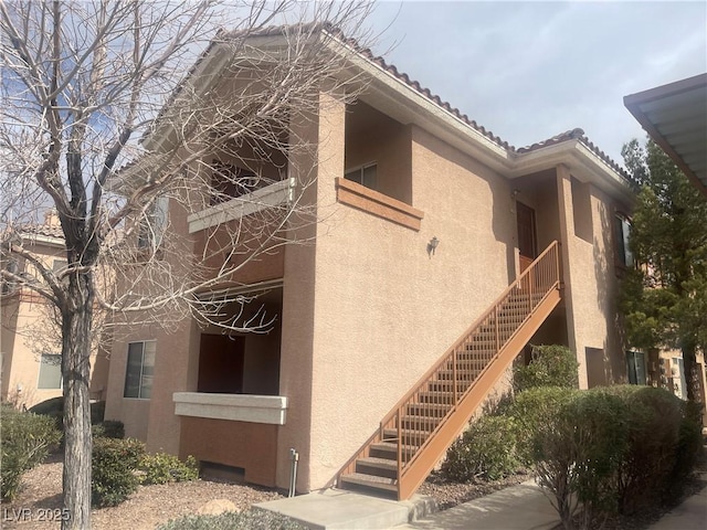 view of home's exterior featuring a tile roof, stairs, and stucco siding