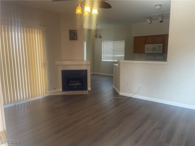 unfurnished living room featuring baseboards, ceiling fan with notable chandelier, wood finished floors, and a fireplace
