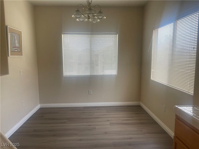 empty room with baseboards, wood finished floors, and a chandelier