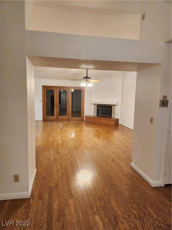 unfurnished living room with a glass covered fireplace, baseboards, ceiling fan, and wood finished floors