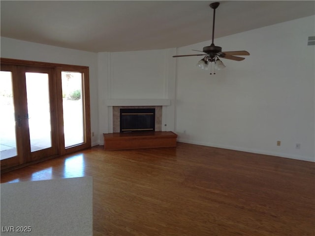 unfurnished living room with ceiling fan, french doors, wood finished floors, baseboards, and a glass covered fireplace