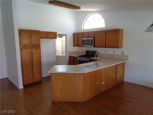 kitchen featuring dark wood-style flooring, a peninsula, light countertops, brown cabinets, and appliances with stainless steel finishes