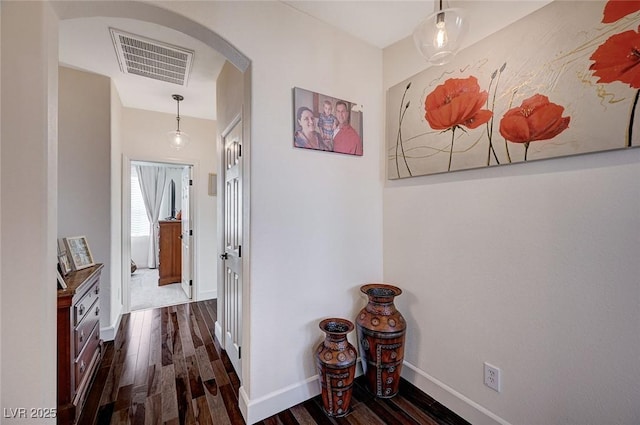 hallway featuring arched walkways, baseboards, visible vents, and dark wood-style floors