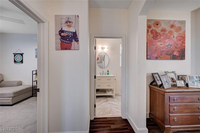 corridor with baseboards, arched walkways, a sink, and dark wood-style floors