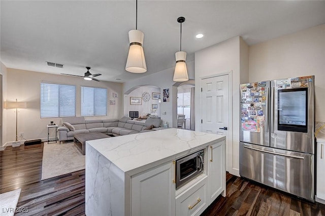 kitchen featuring visible vents, dark wood-style floors, light stone counters, arched walkways, and appliances with stainless steel finishes