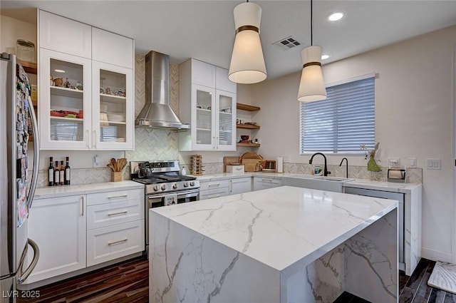 kitchen with light stone countertops, wall chimney range hood, dark wood-type flooring, a sink, and stainless steel appliances