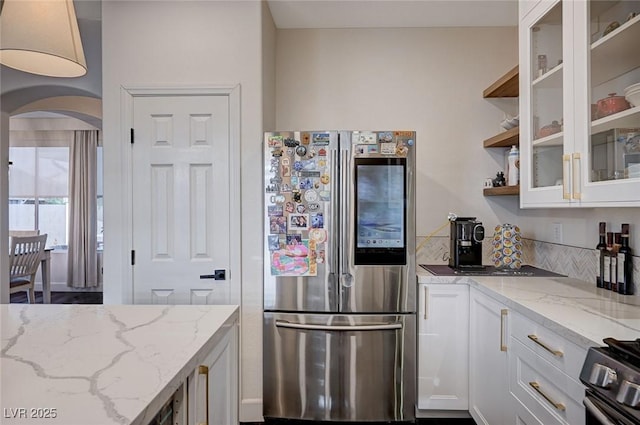 kitchen featuring light stone countertops, glass insert cabinets, white cabinetry, arched walkways, and stainless steel appliances
