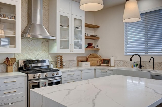 kitchen with decorative backsplash, stainless steel range with gas stovetop, white cabinetry, a sink, and wall chimney exhaust hood