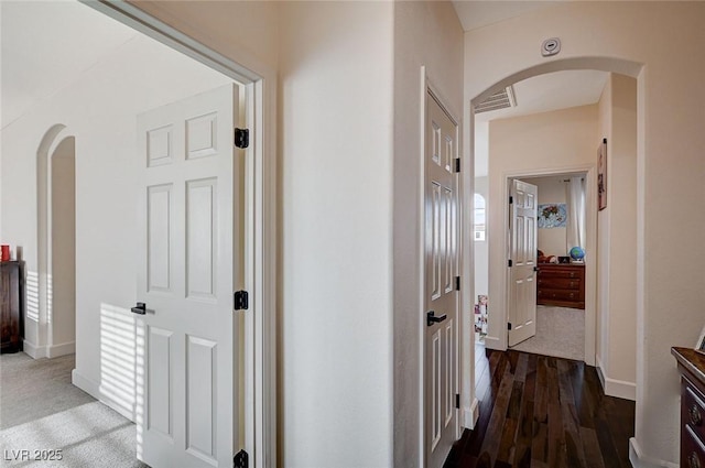 corridor featuring visible vents, wood finished floors, baseboards, arched walkways, and carpet