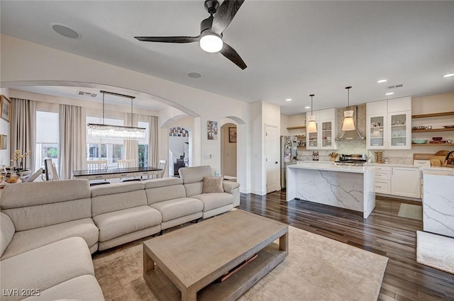 living room featuring visible vents, dark wood-type flooring, recessed lighting, arched walkways, and ceiling fan with notable chandelier