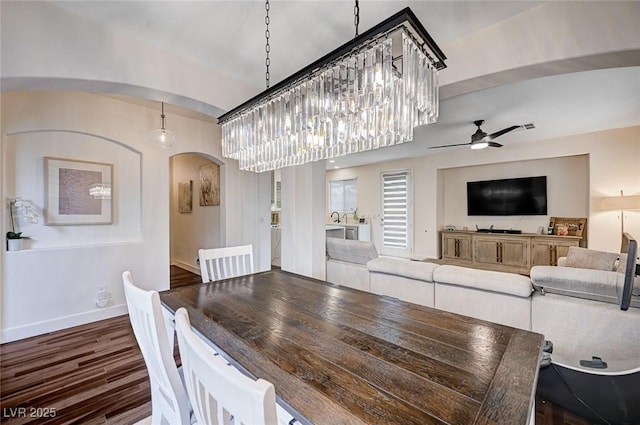 dining space with arched walkways, baseboards, a ceiling fan, and dark wood-style floors