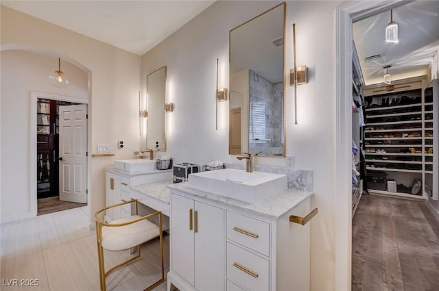 bathroom featuring a sink, a walk in closet, wood finished floors, and two vanities