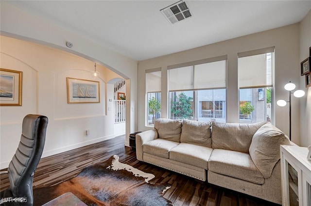 living room featuring arched walkways, baseboards, visible vents, and wood finished floors