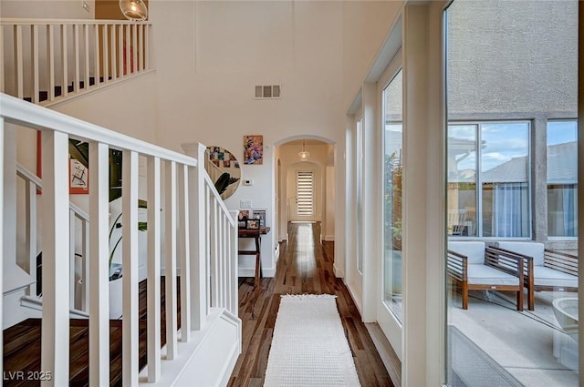 interior space with visible vents, stairs, wood finished floors, a high ceiling, and arched walkways