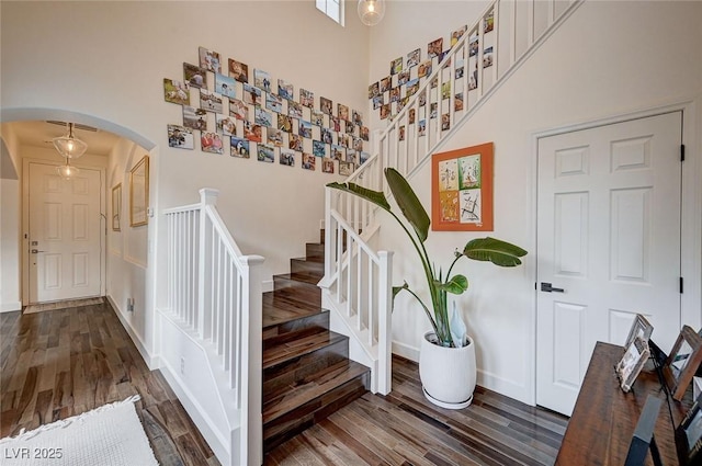stairs featuring arched walkways, a high ceiling, and wood finished floors