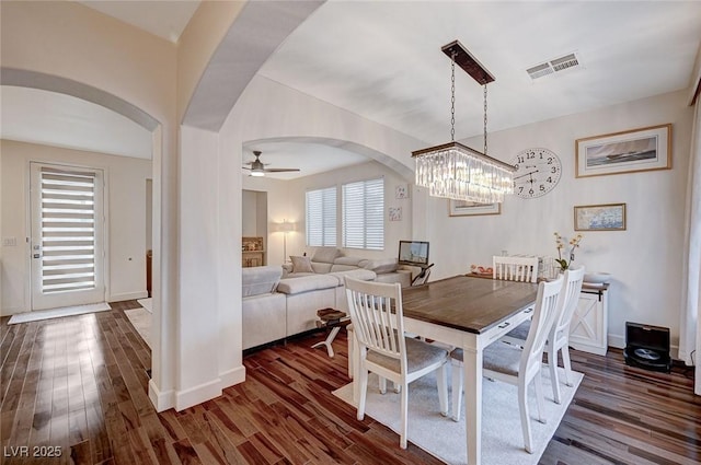 dining area with dark wood-style flooring, visible vents, arched walkways, baseboards, and ceiling fan with notable chandelier