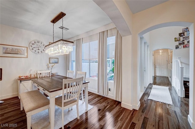 dining room featuring an inviting chandelier, arched walkways, baseboards, dark wood-type flooring, and visible vents