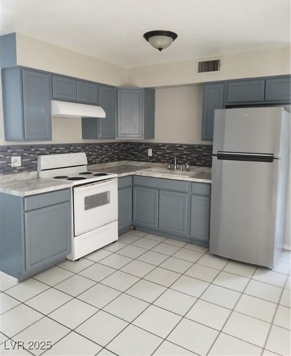 kitchen featuring freestanding refrigerator, under cabinet range hood, backsplash, light countertops, and electric range