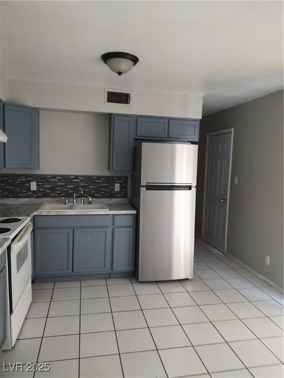 kitchen featuring freestanding refrigerator, gray cabinetry, visible vents, a sink, and white electric range oven