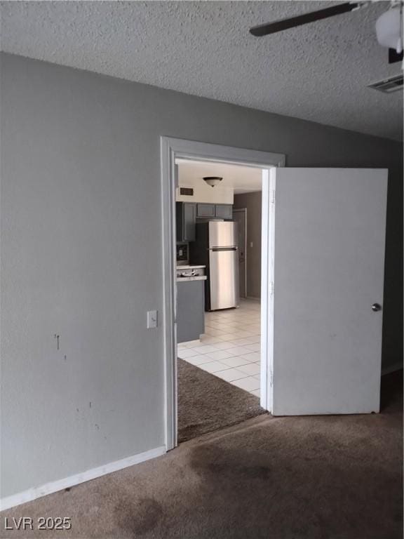 spare room featuring a textured ceiling, light tile patterned floors, a ceiling fan, and light colored carpet