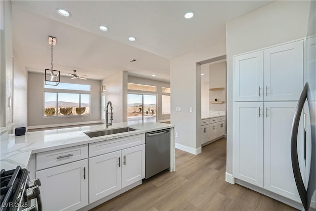 kitchen with a ceiling fan, appliances with stainless steel finishes, a sink, light stone counters, and light wood-style flooring