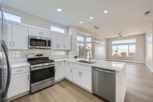 kitchen with visible vents, appliances with stainless steel finishes, light wood-type flooring, a sink, and a peninsula