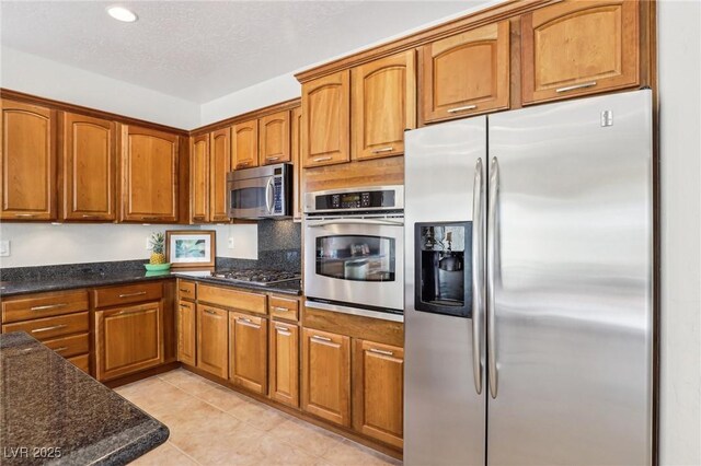 8316 Imperial Lakes St, Las Vegas, NV 89131 - kitchen featuring appliances with stainless steel finishes, brown cabinets, dark stone counters, light tile patterned floors, and recessed lighting