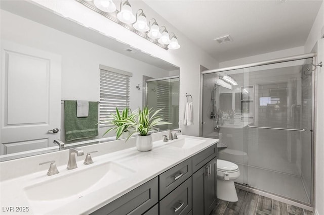 full bathroom featuring double vanity, toilet, a shower stall, and a sink