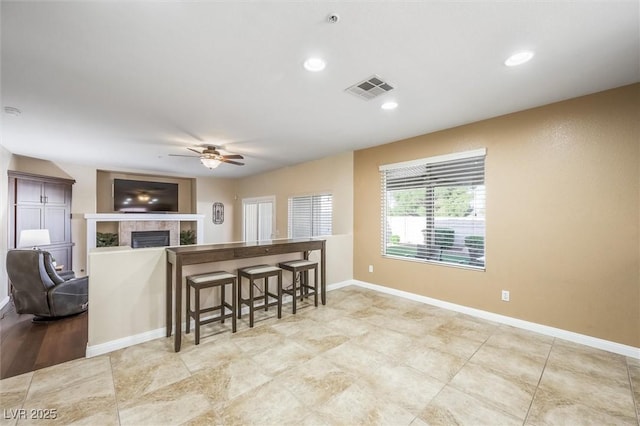 kitchen with ceiling fan, visible vents, a tiled fireplace, baseboards, and open floor plan